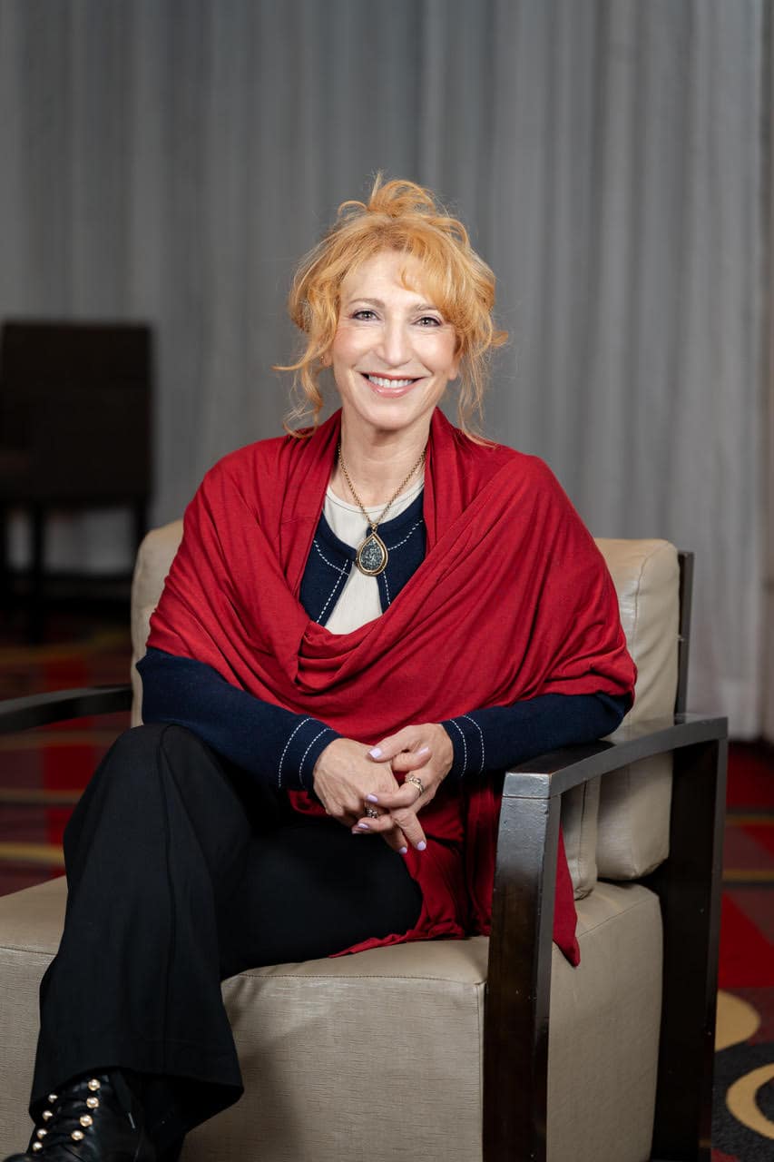 Smiling woman in red shawl sitting on chair.