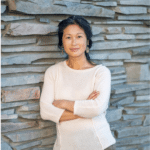 Person standing against stone wall, wearing sweater.