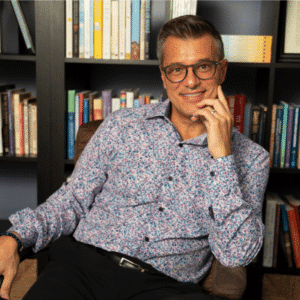 Smiling person sitting, bookshelves in background.