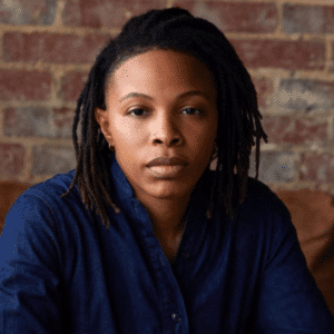 Person in denim shirt against brick wall background.
