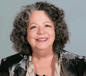Smiling woman with curly hair, wearing floral jacket.