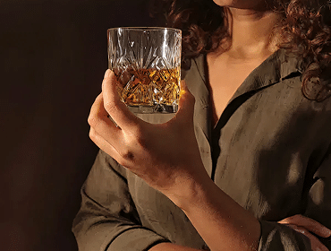 Woman holding glass of whiskey, dark background.